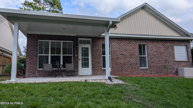 rear view of property featuring a patio, a lawn, and brick siding