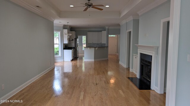 unfurnished living room featuring crown molding, light hardwood / wood-style flooring, sink, a tray ceiling, and ceiling fan