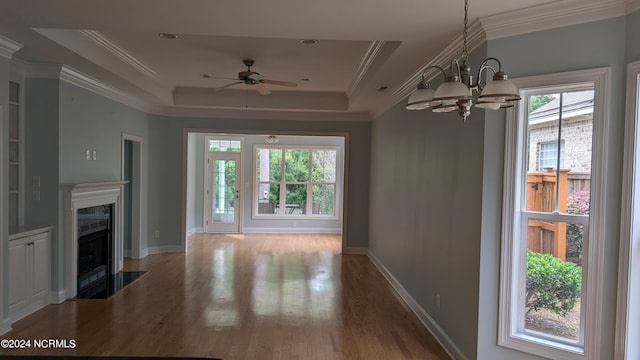 unfurnished living room with a fireplace with flush hearth, a tray ceiling, ornamental molding, and wood finished floors