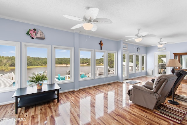 living room with ceiling fan, ornamental molding, a textured ceiling, light wood-type flooring, and a water view