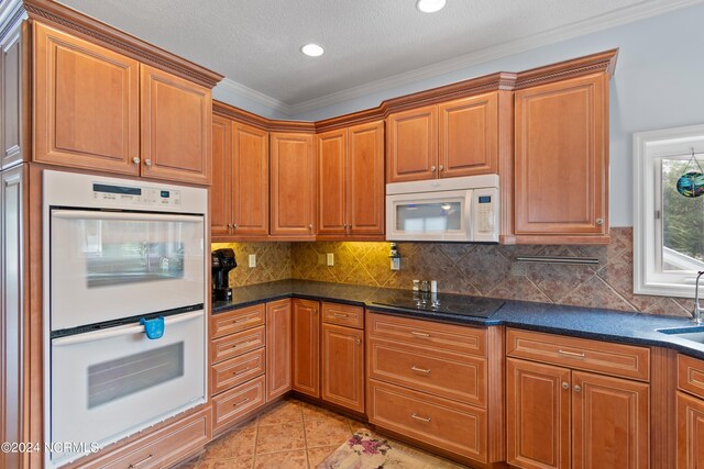 kitchen featuring dark stone countertops, light tile patterned flooring, white appliances, a textured ceiling, and crown molding