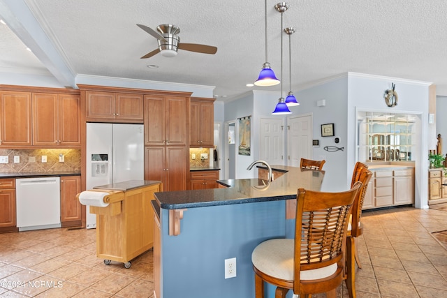 kitchen featuring white appliances, a kitchen bar, ceiling fan, a center island with sink, and ornamental molding