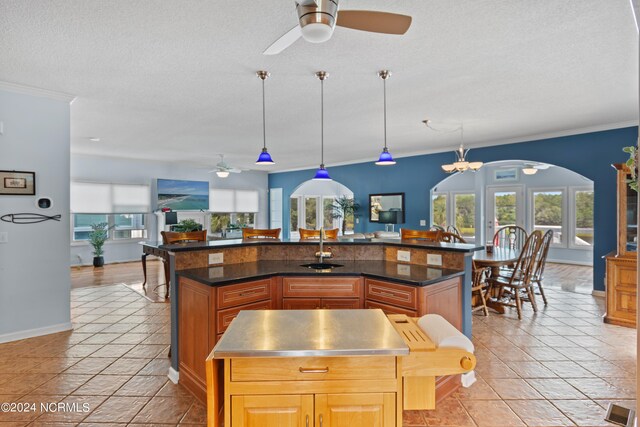 kitchen with hanging light fixtures, ceiling fan with notable chandelier, and a kitchen island with sink