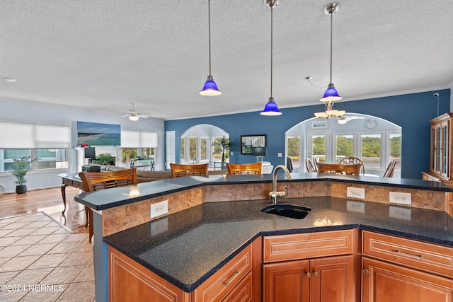 kitchen featuring ceiling fan with notable chandelier, pendant lighting, light wood-type flooring, a textured ceiling, and ornamental molding