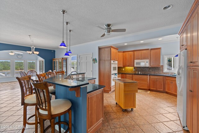 kitchen featuring sink, ornamental molding, white appliances, a center island with sink, and ceiling fan with notable chandelier