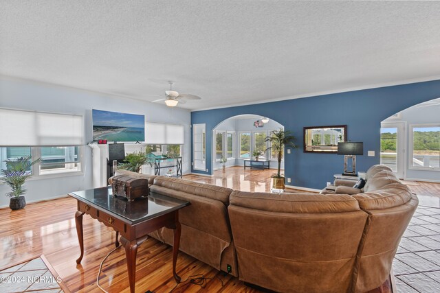 living room featuring light wood-type flooring, ceiling fan, a fireplace, and a textured ceiling