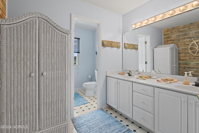 bathroom featuring wooden walls, a textured ceiling, vanity, and toilet