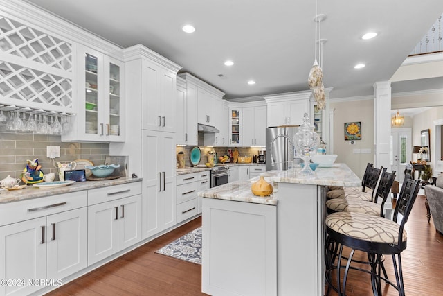 kitchen with appliances with stainless steel finishes, tasteful backsplash, ornate columns, a kitchen island with sink, and dark wood-type flooring