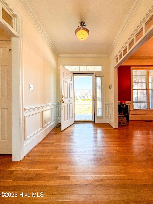 foyer featuring wood finished floors, crown molding, and a decorative wall