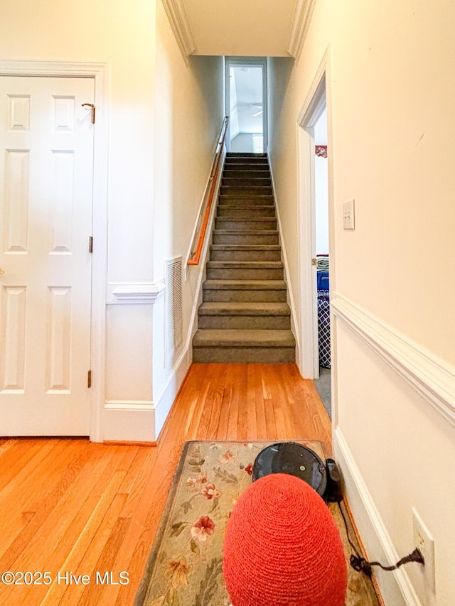 stairs with wood finished floors, visible vents, and ornamental molding