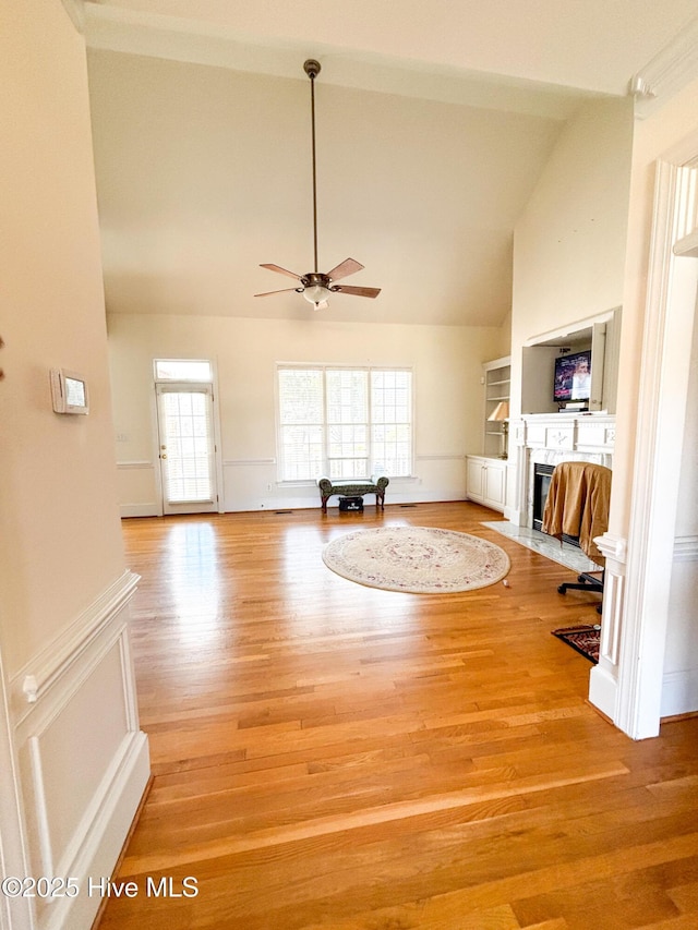 unfurnished living room featuring a decorative wall, a fireplace with flush hearth, a ceiling fan, and light wood-type flooring