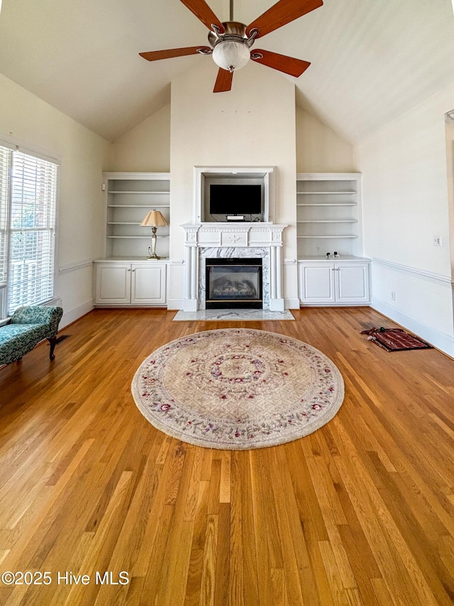 unfurnished living room featuring a high end fireplace, baseboards, wood finished floors, and a ceiling fan