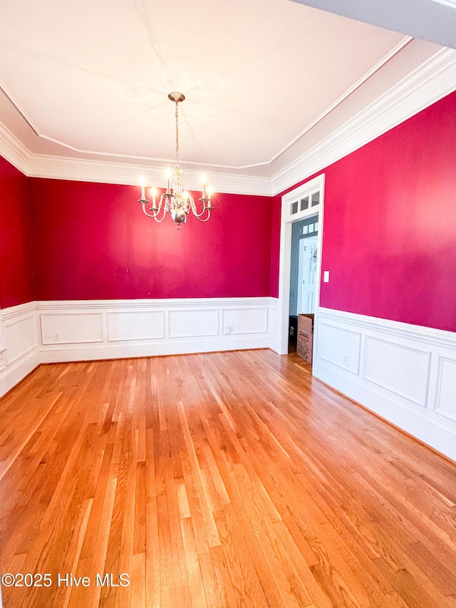 spare room with a chandelier, a wainscoted wall, ornamental molding, and wood-type flooring