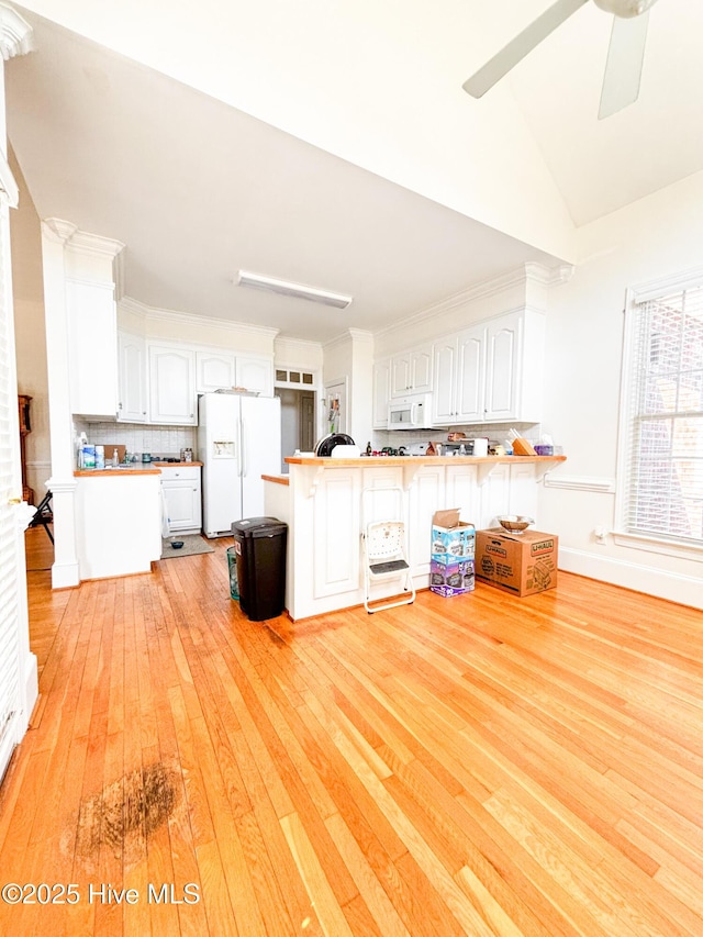 kitchen with tasteful backsplash, light wood-style flooring, a peninsula, white appliances, and white cabinetry