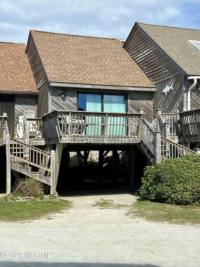 back of property with a shingled roof, stairway, a deck, a carport, and driveway