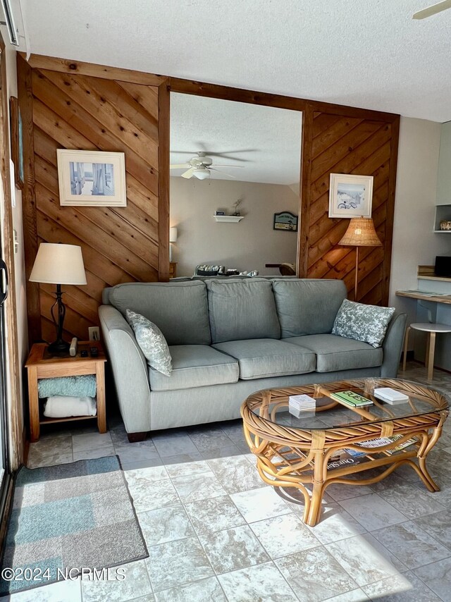 tiled living room featuring ceiling fan, a textured ceiling, and wood walls