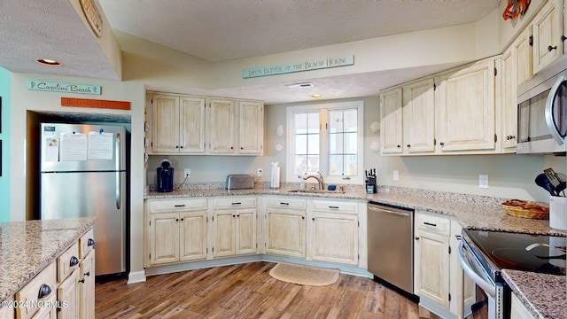 kitchen with light stone countertops, sink, stainless steel appliances, light hardwood / wood-style flooring, and a textured ceiling