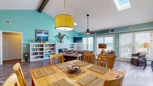 dining space featuring ceiling fan, vaulted ceiling with skylight, a healthy amount of sunlight, and wood-type flooring