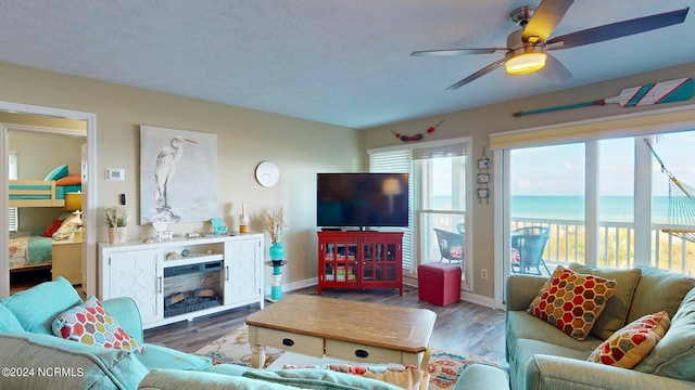 living room featuring a textured ceiling, ceiling fan, a fireplace, and dark wood-type flooring