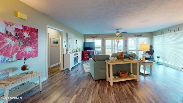 living room with a textured ceiling, ceiling fan, and dark wood-type flooring