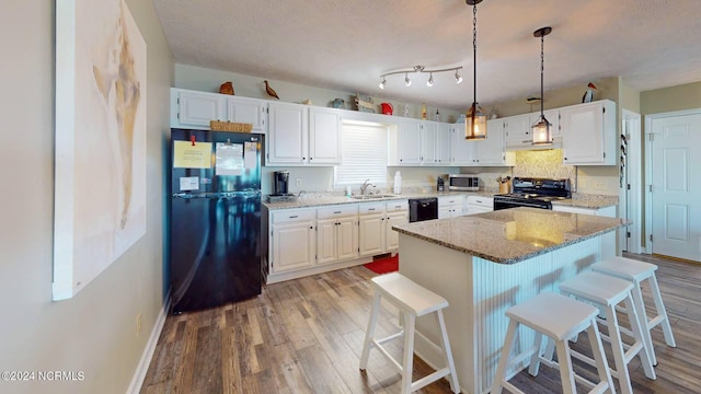 kitchen with light stone countertops, white cabinetry, black appliances, and light hardwood / wood-style floors