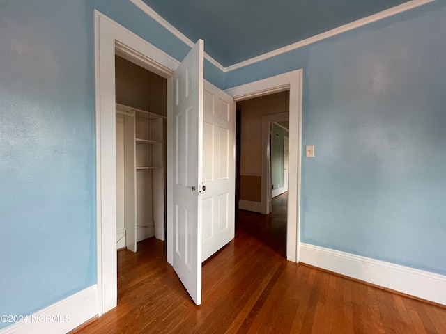 unfurnished bedroom with a closet, crown molding, and dark wood-type flooring