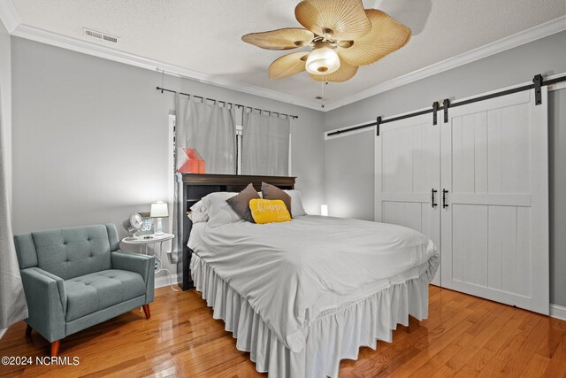 bedroom featuring crown molding, ceiling fan, a barn door, and light hardwood / wood-style floors