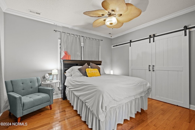 bedroom featuring light wood finished floors, a barn door, visible vents, and crown molding