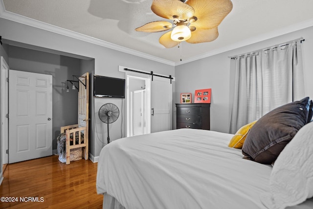 bedroom featuring a ceiling fan, a barn door, ornamental molding, and wood finished floors