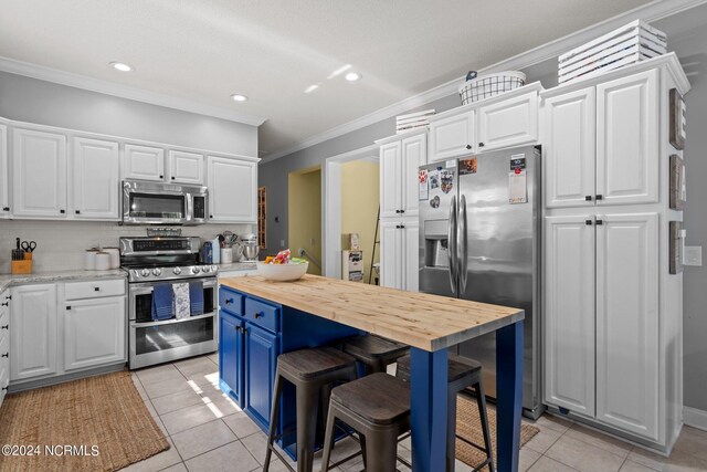 kitchen with stainless steel appliances, white cabinetry, light tile patterned flooring, blue cabinets, and butcher block counters