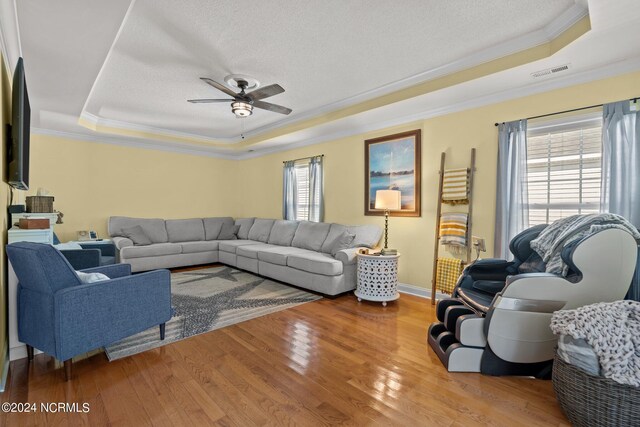 living room with a wealth of natural light, a raised ceiling, and ceiling fan