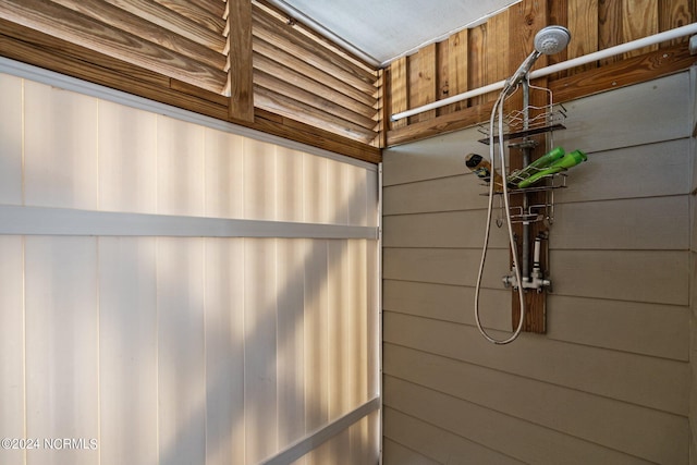 bathroom featuring tiled shower and wood walls