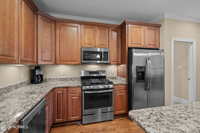 kitchen with light wood-type flooring, appliances with stainless steel finishes, crown molding, and light stone counters