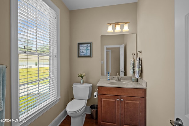 half bath with toilet, vanity, baseboards, and wood finished floors