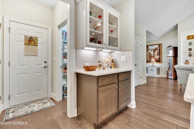 interior space featuring backsplash, light stone countertops, vaulted ceiling, and light hardwood / wood-style flooring