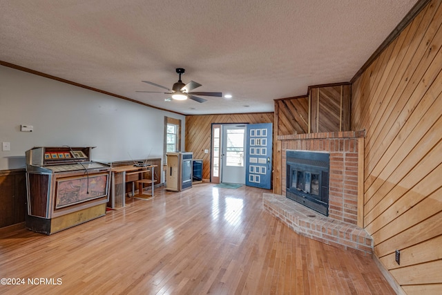 unfurnished living room featuring wood walls, a brick fireplace, hardwood / wood-style floors, crown molding, and ceiling fan