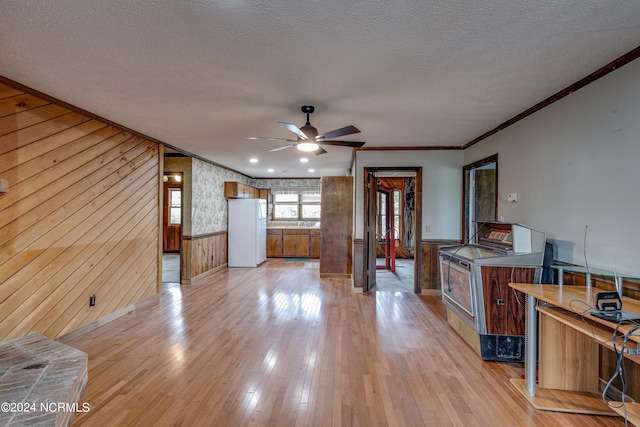 unfurnished living room featuring wooden walls, light hardwood / wood-style floors, ceiling fan, and a textured ceiling