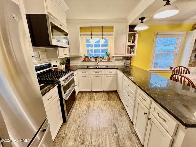 kitchen with light wood-style flooring, stainless steel appliances, a sink, white cabinets, and decorative backsplash