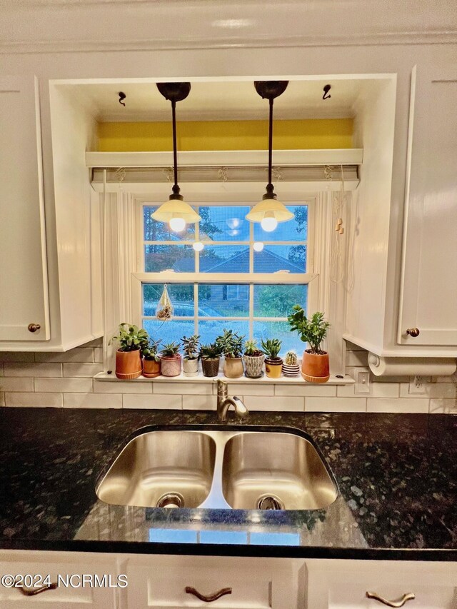 kitchen with white cabinetry, a sink, decorative light fixtures, and dark stone countertops