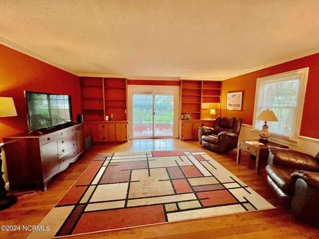 living area with built in shelves, crown molding, a textured ceiling, and wood finished floors