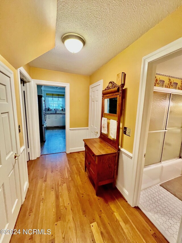 hallway featuring light wood-type flooring and a textured ceiling