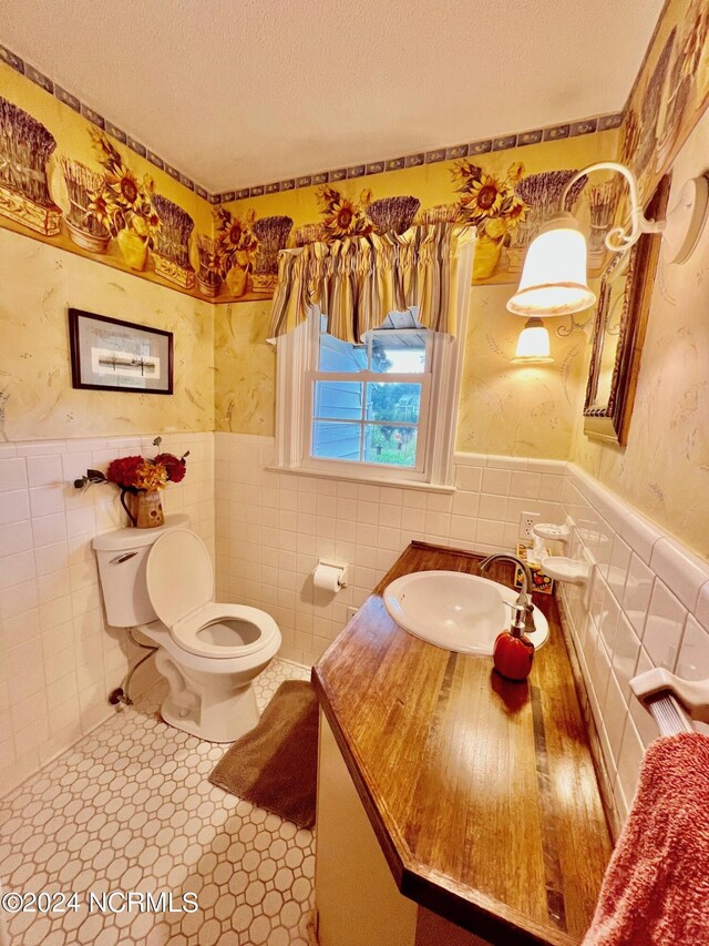 half bath featuring a wainscoted wall, a textured ceiling, toilet, and wallpapered walls