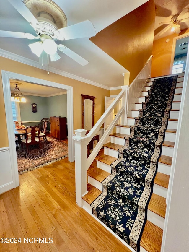 stairs featuring a ceiling fan, ornamental molding, and hardwood / wood-style floors