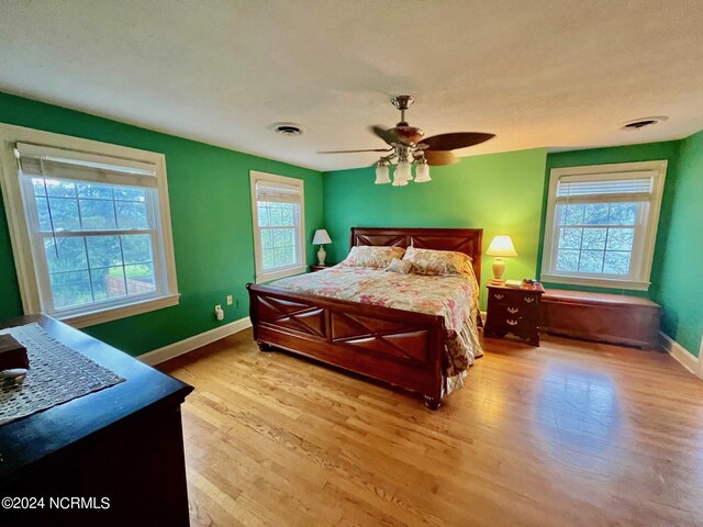 bedroom with a ceiling fan, light wood-type flooring, visible vents, and baseboards