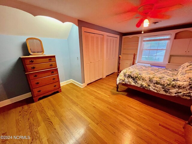 bedroom featuring light wood finished floors, ceiling fan, baseboards, and two closets