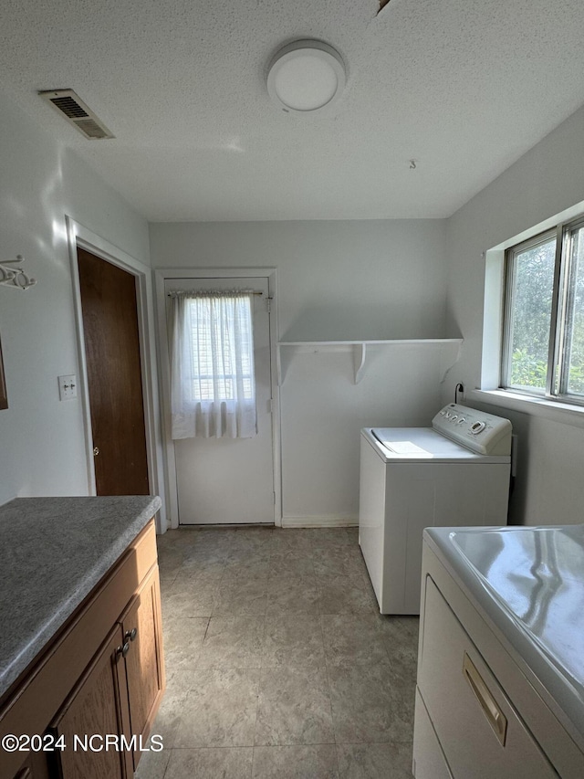 washroom featuring cabinet space, visible vents, a textured ceiling, and washing machine and clothes dryer