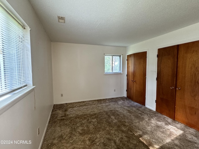 unfurnished bedroom with a textured ceiling, carpet flooring, two closets, and baseboards