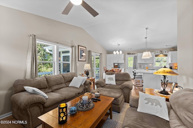 living room featuring vaulted ceiling, ceiling fan with notable chandelier, and wood-type flooring