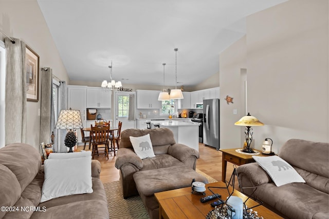 living room featuring high vaulted ceiling, an inviting chandelier, and light hardwood / wood-style flooring