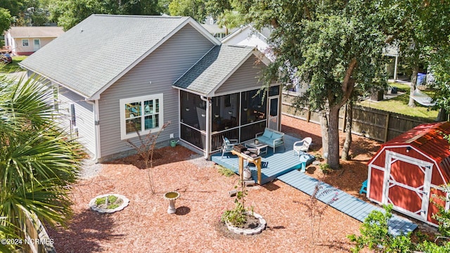 rear view of house featuring a sunroom, fence, a deck, a storage unit, and an outdoor structure